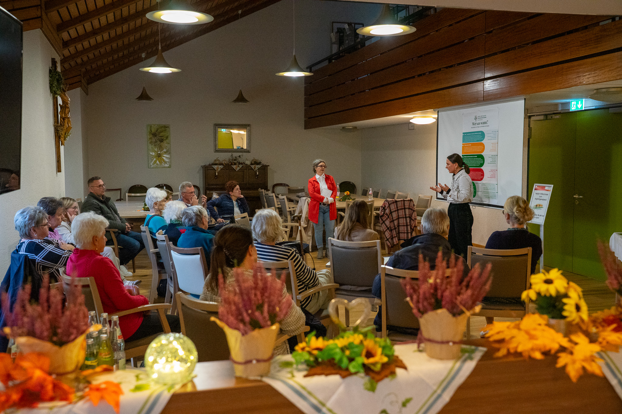 Eine Gruppe Menschen in einem Saal hört zwei Rednerinnen zu.