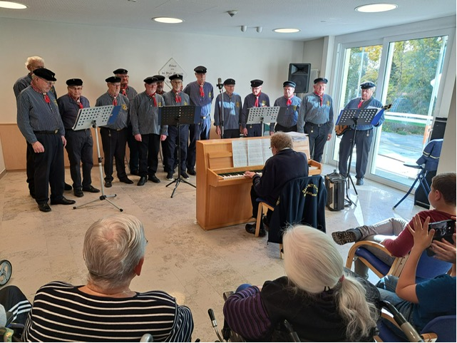 Gruppe Menschen in Seemannskostümen steht hinter Pianisten in einem Raum des Seniorenheimes