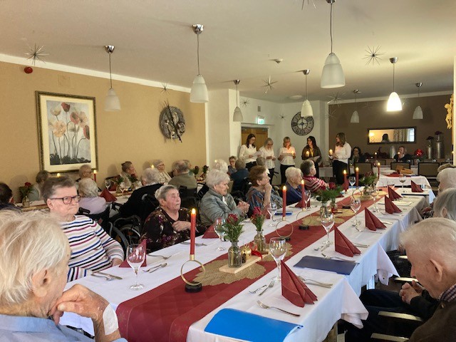 Viele Menschen an einem großen Tisch, im Hintergrund ein Chor