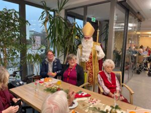 Nikolaus mit drei Menschen an einem festlich geschmückten Tisch