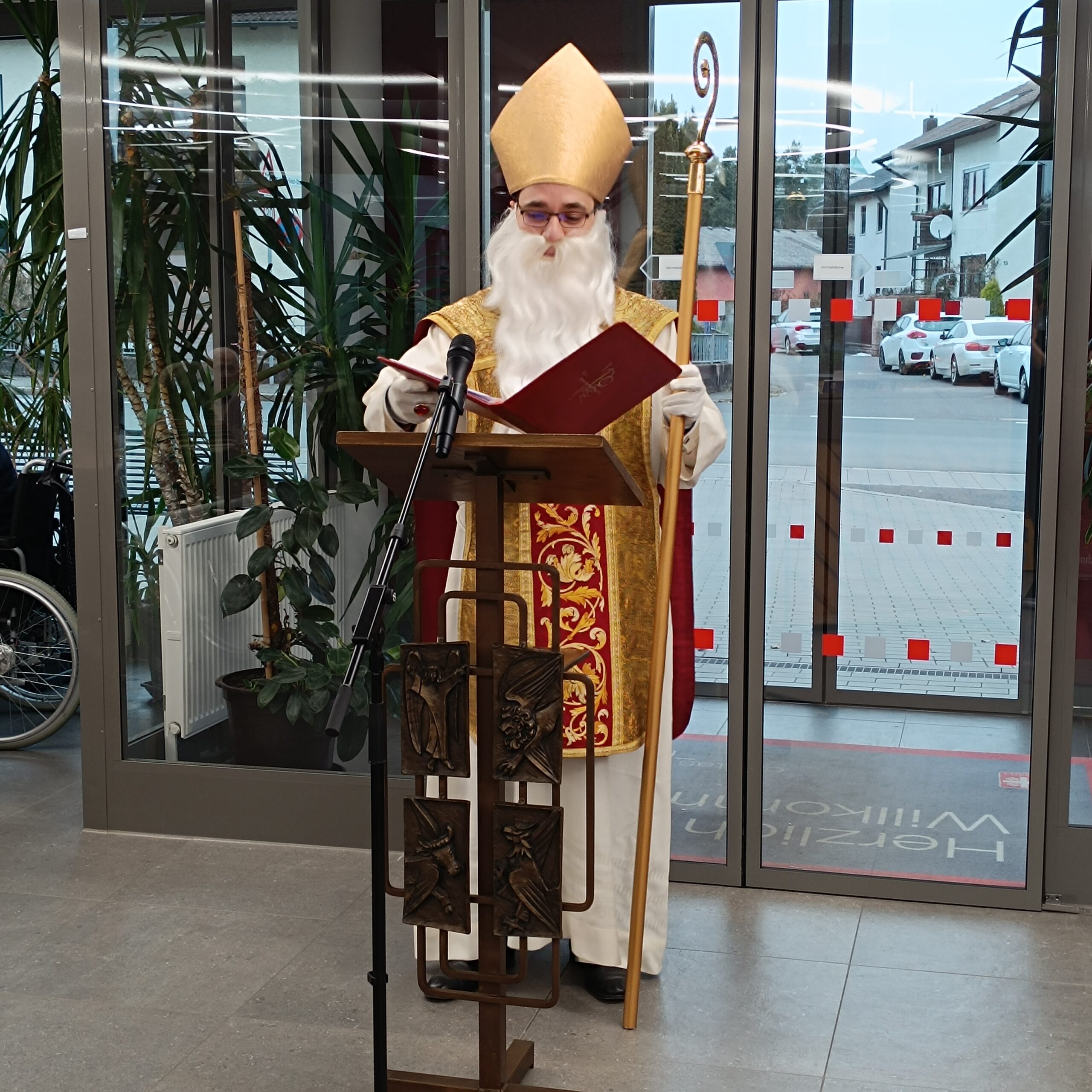 Nikoluas vor dem Eingang hinter einem Rednerpult mit Buch in der Hand