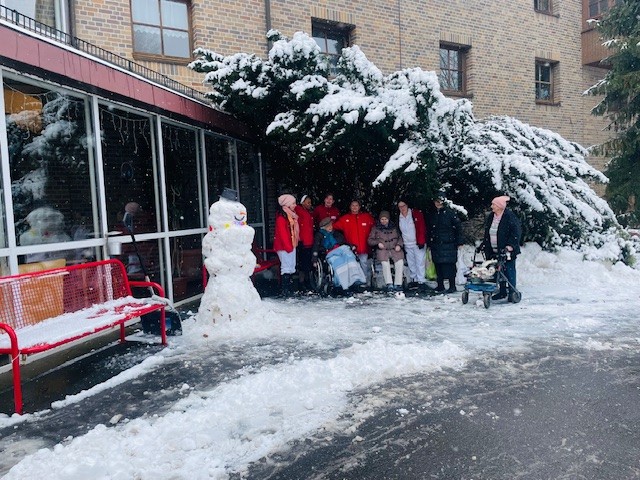 Außenaufnahme vor einem Altenheim. Viele Personen neben einer Schneefrau.