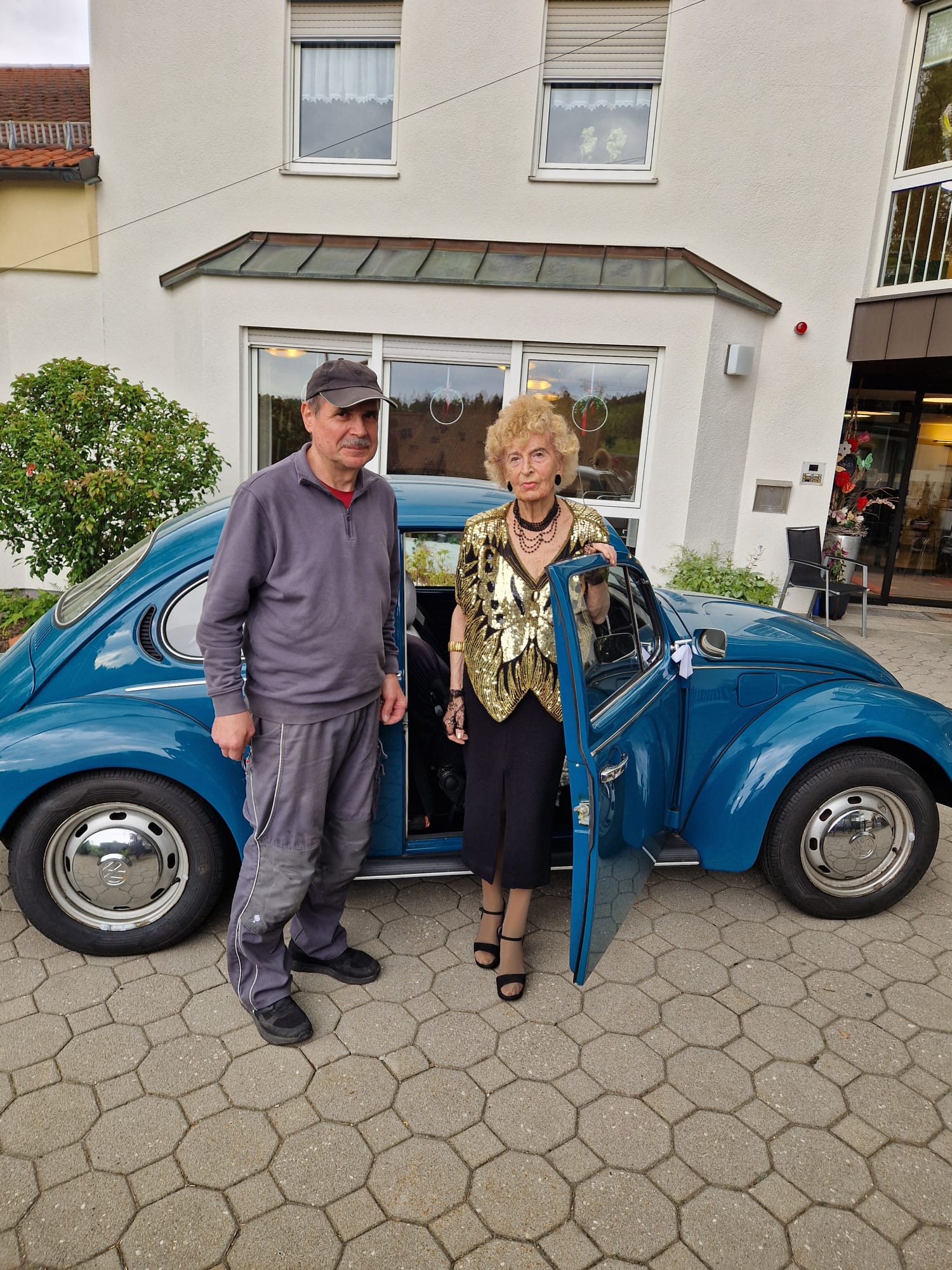 Zwei Personen vor blauem VW Käfer