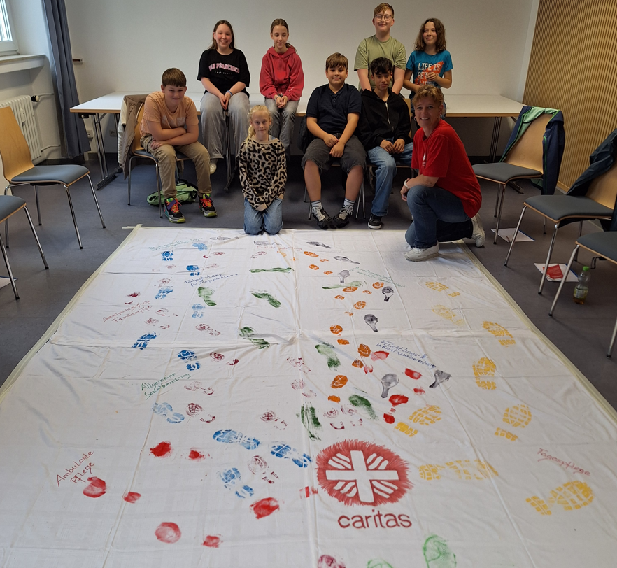 Gruppe vor großem Teppich mit Fußspuren und Handabdrücken und Caritas Logo